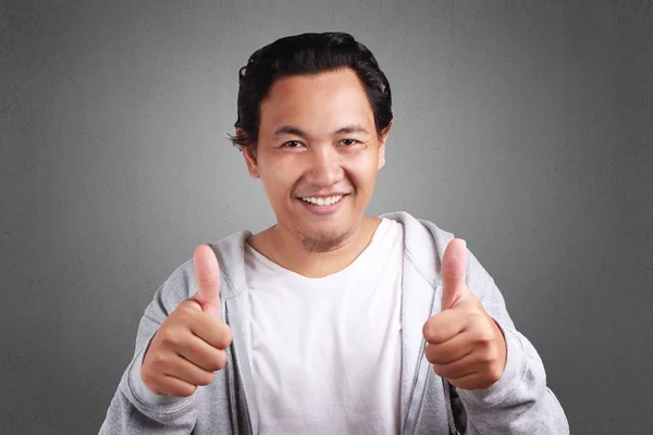 アジア系の若い男を持ち上げ つの親指とジャケットを着て笑顔の優しい — ストック写真