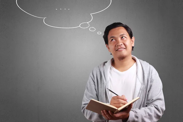 Young Asian man wearing white shirt and gray jacket holding a book with thinking sign. Background on gray. Close up body portrait