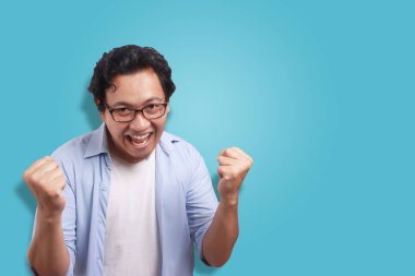 Küçük Asya adam giyen beyaz ve mavi gömlek mutlu ifade, zafer jest kutluyor. Beyaz izole. Vücut portre kadar kapatın