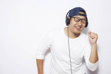 Fotoğraf resim mutlu komik Genç Asyalı adamın şapka ve kulaklık ile müzik dinleme sırasında dans gözlük takıyor. Beyaz duvara karşı