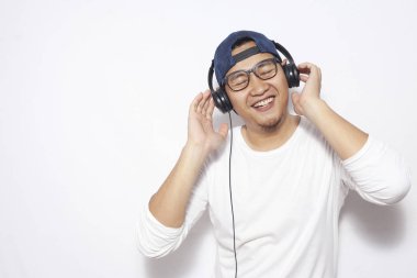 Fotoğraf resim mutlu komik Genç Asyalı adamın şapka ve kulaklık ile müzik dinleme sırasında dans gözlük takıyor. Beyaz duvara karşı