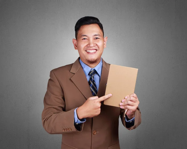 Portrait of young businessman holding and showing a book, empty cover template mock up, over grunged wall background