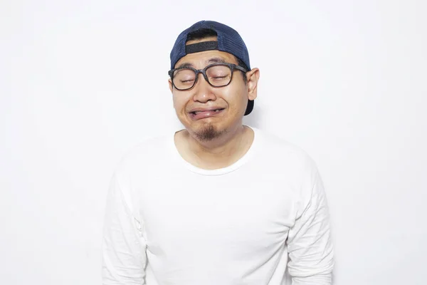 Portrait of funny sad Asian man wearing hat and eyeglasses crying hard over white background