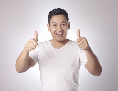 Fotoğraf resim portre komik çekici şirin Asyalı gencin gülümseyen ve başparmak yukarıya işareti, yarım vücut portre gri arka plan üzerinde gösterilen beyaz gömlekli