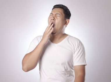 Esneme, otururken, yarım vücut portre gri arka plan üzerinde uyku uykulu yorgun komik Genç Asyalı adam