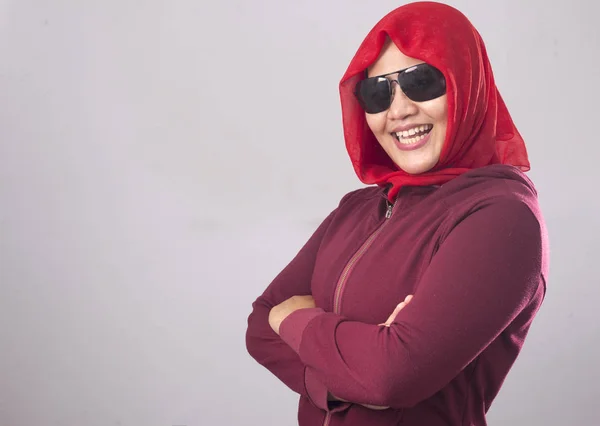 Portrait of confidence muslim lady wearing black sunglasses in red suit and hijab smiling with crossed arms