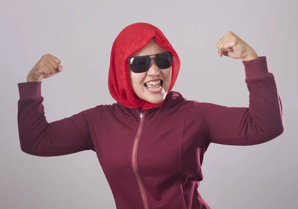 赤いスーツとヒジャーブに黒のサングラスをかけてアジアのイスラム教徒の女性の肖像画は強力な筋肉力ジェスチャーを示しています — ストック写真