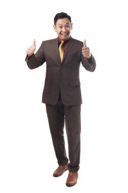 Kahverengi resmi elbise giymiş genç Asyalı işadamı jest, yukarı mutlu gülümseyen iyi jest, tam vücut portre üzerinde beyaz izole memnun gösterir