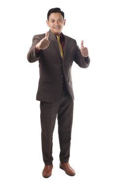 Kahverengi resmi elbise giymiş genç Asyalı işadamı jest, yukarı mutlu gülümseyen iyi jest, tam vücut portre üzerinde beyaz izole memnun gösterir