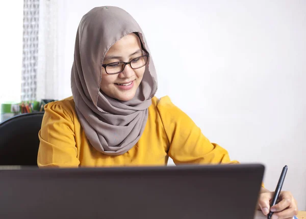 オフィスのノートパソコンで働くアジア系ムスリムのビジネスマンの姿が笑顔で表現されています — ストック写真
