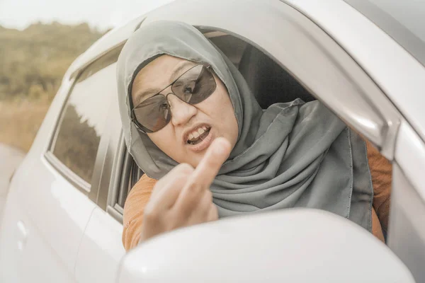 Portrait of Asian muslim lady driver getting mad and angry from the traffic, screaming and showing rude gesture from her car
