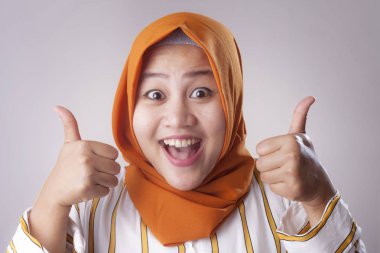 Başörtüsü takan genç Asyalı Müslüman kadının portresi baş parmak işareti, gülen surat, onaylanmış işaret.