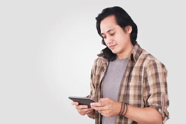 一个可爱英俊的年轻亚洲男子的肖像 长发和有趣的脸在平板电脑上玩游戏 — 图库照片