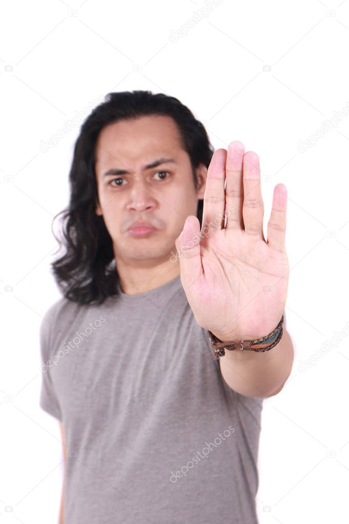 Portrait of good looking long haired young Asian man shows stop gesture with his finger isolated on white