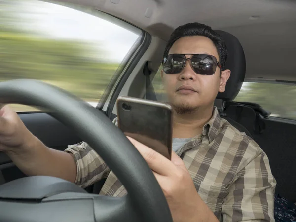 Conductor masculino leyendo el mensaje en el teléfono inteligente mientras conduce un coche —  Fotos de Stock