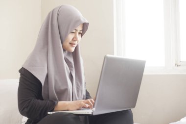 Yatak odasında dizüstü bilgisayar ile çalışan mutlu Müslüman kadın