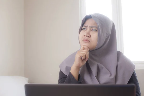 Muslimische Geschäftsfrau arbeitet zu Hause am Laptop, denkende Geste — Stockfoto