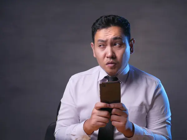 Joven hombre pensando mientras charla en el teléfono inteligente — Foto de Stock