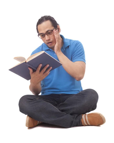 Mladý muž sedící na podlaze a čtení knihy, šokované gesto — Stock fotografie