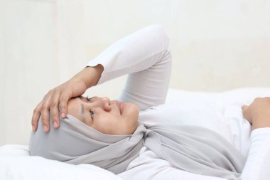 Üzgün, Asyalı Müslüman kadın boş bakışlarla yatakta uzanıyor, kötü durumu düşünerek uyumak zor, duygusal ifade.