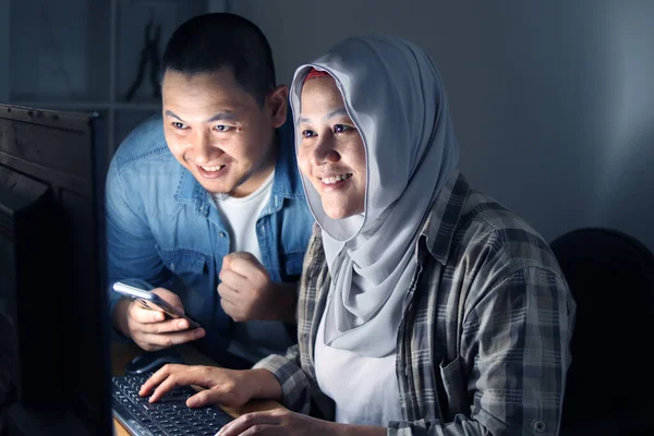 Couple reading a contract received by email at night, checking details and connecting online with their computer, happy smiling successful gesture