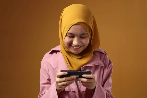 若いですアジアのイスラム教徒の十代の少女の肖像画とともにスマートフォン 黄色の背景に彼女の携帯電話でオンラインチャットメッセージを読むときに喜んで笑顔 — ストック写真