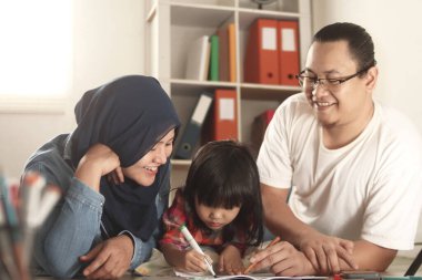 Asyalı Müslüman ebeveynler kızlarıyla resim çiziyorlar, anne ve babaları bebeklerine öğretiyor, yerde öğreniyorlar, mutlu aile kavramları.  