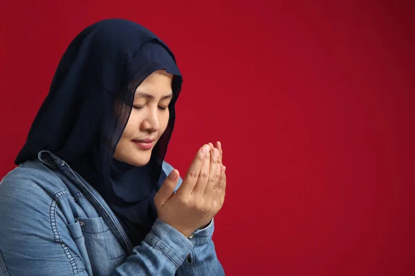 Asian muslim woman prays to God, praying gesture hands raised up, Islam religion spiritual life, over red background