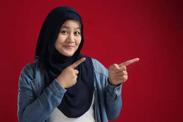 Portret Azjatki Młodej Szczęśliwej Muzułmanki Wskazującej Coś Boku Czerwonym Tle — Zdjęcie stockowe