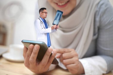 Çevrimiçi sağlık hizmetleri kavramı, Asyalı erkek doktorla akıllı telefon uygulamasını gösteriyor. Röntgenleri ve gülümseyen kadını, teletıp görüntülerini kontrol ediyor.
