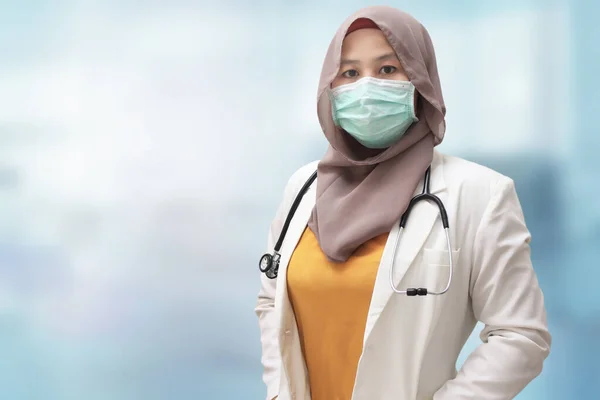 Muslim female doctor wearing hijab and suit, standing with protective face mask , ready to fight coronavirus covid19 global pandemic