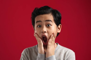 Kameraya bakan komik Asyalı bir çocuğun portresi. Ağzı açık ve büyük gözlü. Kırmızı arka planda şaşırmış bir ifade.