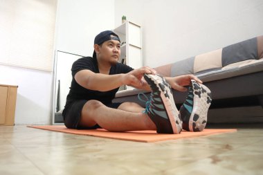 Asyalı erkek, yeni normal yaşam tarzında sağlıklı kalmak için evde egzersiz yapıyor, evde egzersiz yapıyor, esneklik için esneme hareketleri yapıyor.