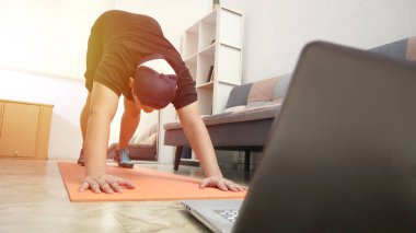 Asyalı erkek evde egzersiz yaparken dizüstü bilgisayarda video eğitimi, ev içi antrenman konsepti izliyor, yeni normal yaşam tarzına sağlıklı bakıyor.