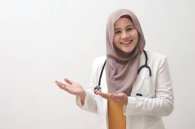 Gülümseyen genç, Asyalı Müslüman kadın doktor beyaz arka planda izole edilmiş ve yanında fotokopi alanı olan bir şey gösterip sunuyor.
