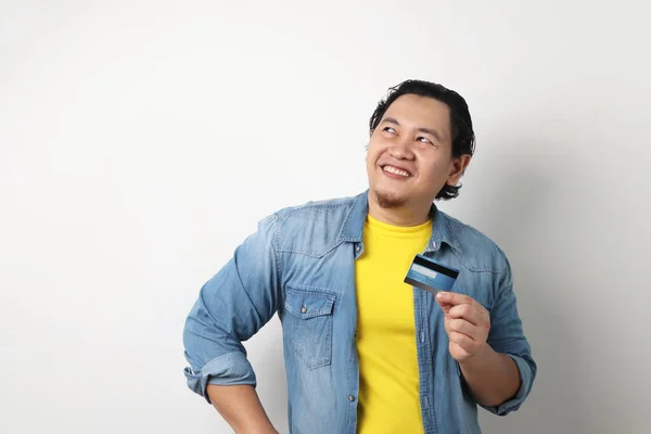 Portrait of happy susseccful young Asian man smiling and thinking while holding a credit card