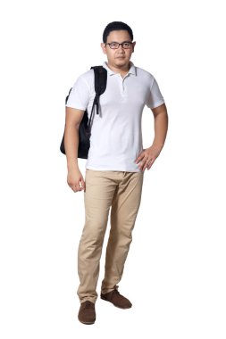 Genç Asyalı erkek öğrenci kameraya özgüvenle bakıyor sırt çantası tutarken gülümsüyor. Tüm vücut portresi beyaza izole edilmiş.