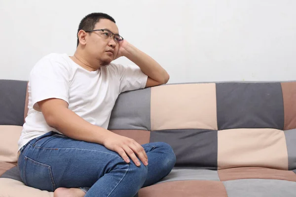 自宅のリビングルームで彼のソファの上に座って考えている不幸なアジアの男 悲しい心配そうな表情 — ストック写真