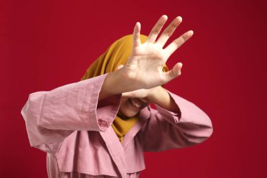 Genç müslüman genç kız tesettüre bürünmüş ağlıyordu ve yüzünü kapatıyordu, endişeli bir ifade vardı, baskı altında eziliyordu, kırmızı arka plana karşı durmak istiyordu.