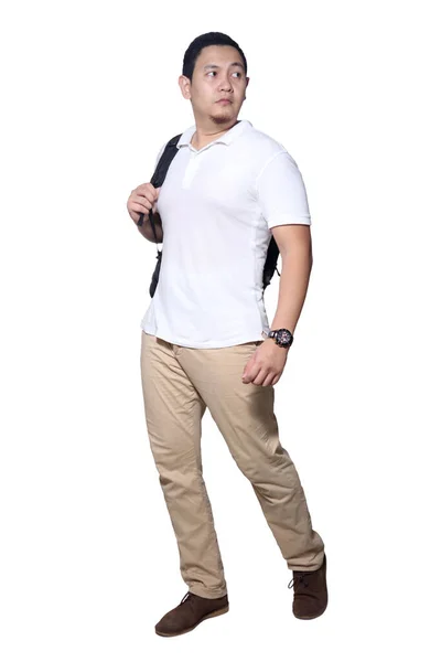 白いシャツを着たアジア人男性の完全な長さの肖像画 カーキジーンズとバックパック立って歩く 白に隔離されたサイドビュー — ストック写真