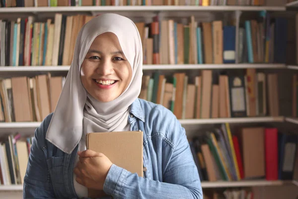 Asian muslim woman wearing hijab reading book in library, educational concept. Happy smiling expression when doing leisure activity