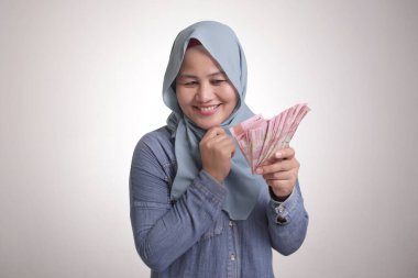 Endonezyalı Müslüman kadının portresi rupiah parası taşıyor, gülümsüyor ve düşünüyor.