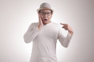 Asyalı bir adam kendini mutsuz bir ifadeyle işaret ediyor. Sanki suçlandığı için kafası karışmış ve kime sormuş gibi. Ben.?