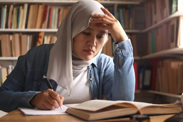 Asian muslim woman studying learning in library, exam preparation concept. Female college student doing research and making notes in her book