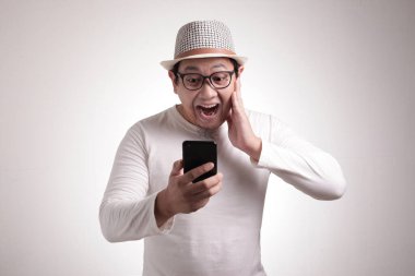 Çekici Asyalı genç adam telefonunda mesajlaşan mesajları okuyor, şaşırmış yüz ifadesi.