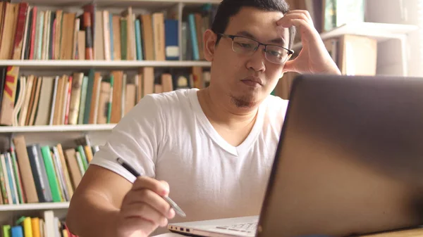 Asian muslim man studying in library, exam preparation concept. Male college student doing research and using laptop to learn online