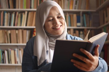 Kütüphanede tesettürlü Asyalı Müslüman kadın kitap okuyor, eğitici bir kavram. Boş zamanlarında gülen mutlu yüz ifadesi