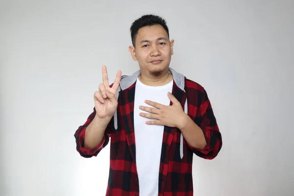 Portrait of happy Asian man making pledge gesture, hand on chest holding heart, making promise