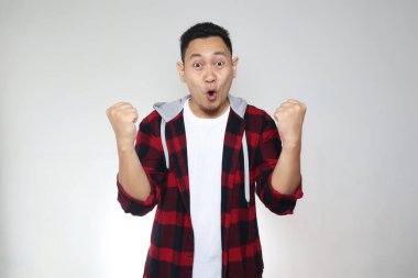 Başarılı genç Asyalı adam zafer kutlamalarında zafer jesti gösteriyor. Ellerini havaya kaldır ve mutlu bir yüz yap.