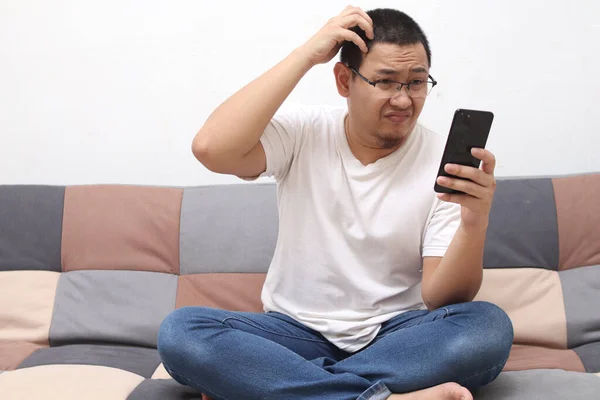 Confuso Asiático Homem Coçar Cabeça Quando Olhando Para Telefone Enquanto — Fotografia de Stock